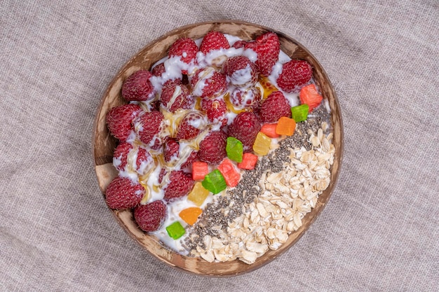 Frullato in ciotola di cocco con lamponi farina d'avena frutta candita e semi di chia per colazione primo piano Il concetto di mangiare sano superfood