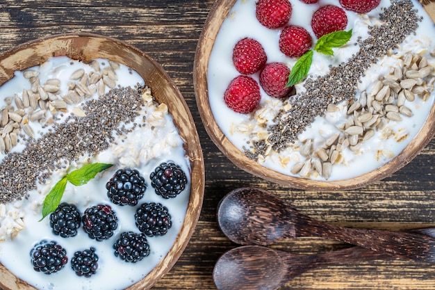 Frullato in ciotola di cocco con more, lamponi, farina d'avena, semi di girasole e semi di chia per colazione da vicino Il concetto di mangiare sano superfood