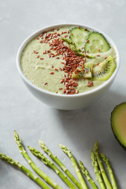 Frullato verde di asparagi di kiwi e cetriolo di avocado con semi di lino in una ciotola bianca su fondo grigio