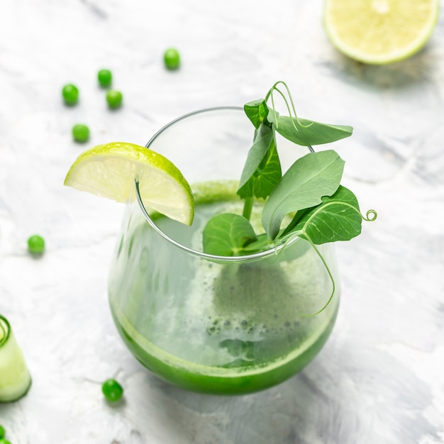 Frullato verde fresco Bevanda sana e disintossicante con foglie verdi di cavolo verde piselli freschi, cetriolo, spinaci e lime su sfondo bianco.
