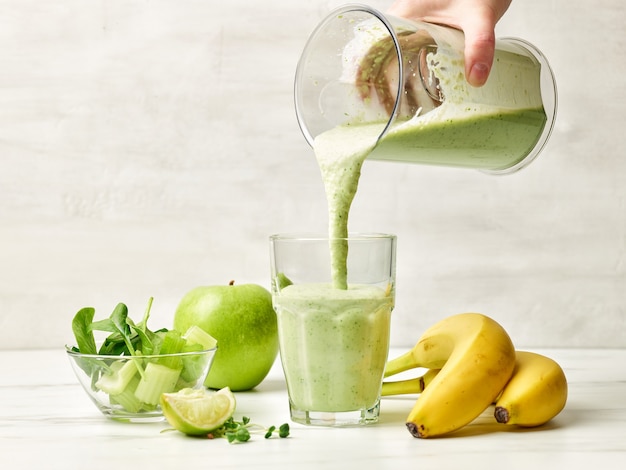 Frullato verde fresco che versa nel bicchiere pronto per una sana colazione