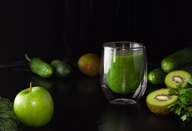 Frullato verde in un bicchiere di vetro su sfondo nero. Kiwi, mele, cetrioli e verdure. Cucinare cibi sani.