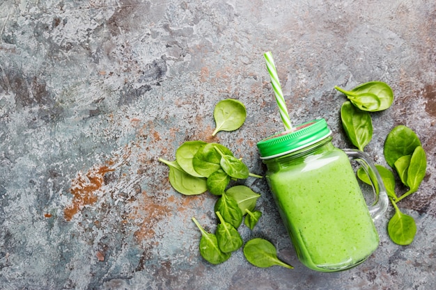 Frullato verde sano con spinaci, avocado, banana e semi di chia in barattoli di vetro su fondo di pietra grigia, vista dall'alto.