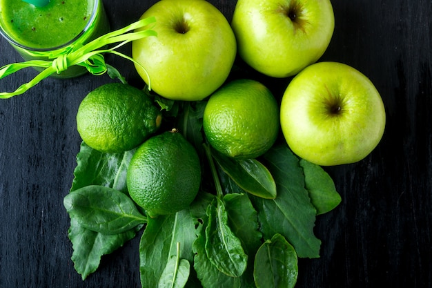 Frullato verde vicino agli ingredienti per su fondo di legno nero. Mela, lime, spinaci. Detox. Bevanda salutare