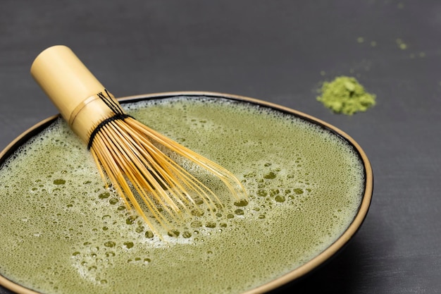 Frusta di bambù in una ciotola nera con tè verde matcha