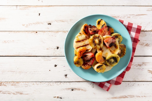 Frutta alla griglia sulla zolla blu e sulla tavola di legno bianca