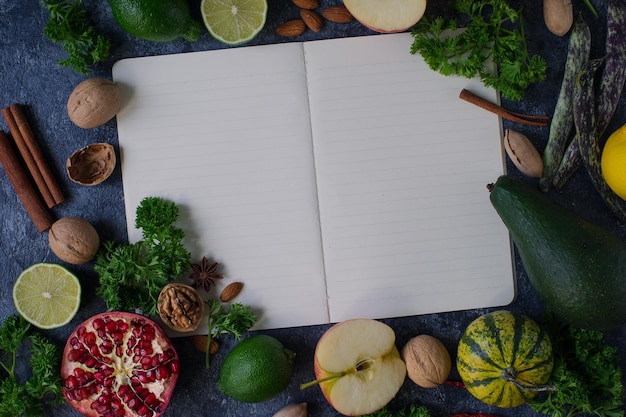 Frutta biologica cruda verdure verdi noci e ricettario su tavola di pietra scura concetto di cibo sano dieta e spazio per mangiare pulito per il testo