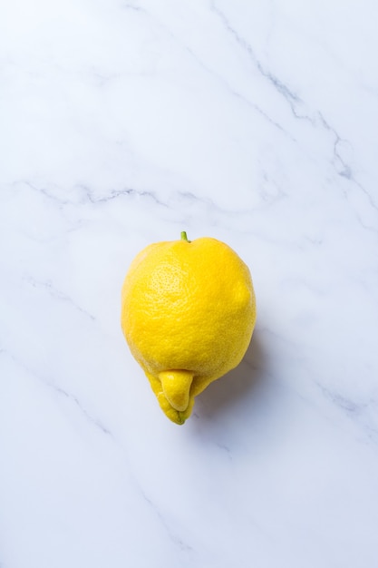 Frutta brutta alla moda, limone giallo succoso divertente con forma imperfetta su un tavolo di marmo bianco. Gli agricoltori producono uno strano concetto di spreco alimentare organico e deforme. Vista dall'alto, copia lo sfondo dello spazio