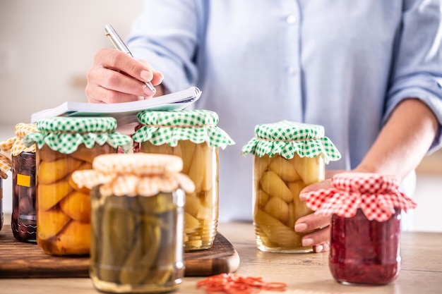 Frutta conservata fatta in casa e verdure sott'aceto con una donna che scrive la ricetta sullo sfondo.