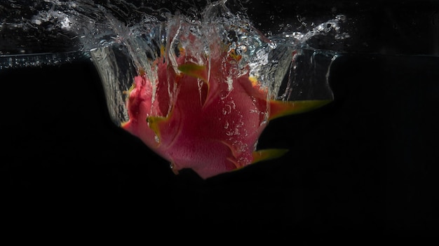 FRUTTA DEL DRAGO O PITAHAYA CHE FANNO SPRUZZARE IN ACQUA CON SFONDO NERO E SENSAZIONE DI MOVIMENTO