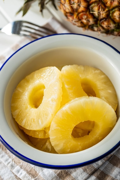 Frutta di ananas a fette in scatola in una ciotola sul tavolo bianco