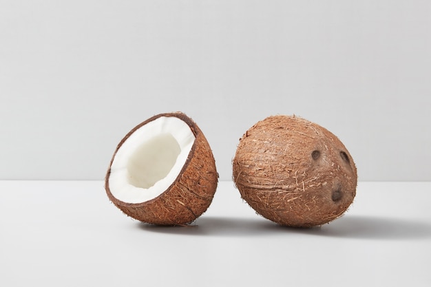 Frutta di cocco matura esotica naturale con intero uno e mezzo di dado su uno sfondo grigio chiaro a due tonalità con ombre morbide, copia dello spazio. Concetto vegano.