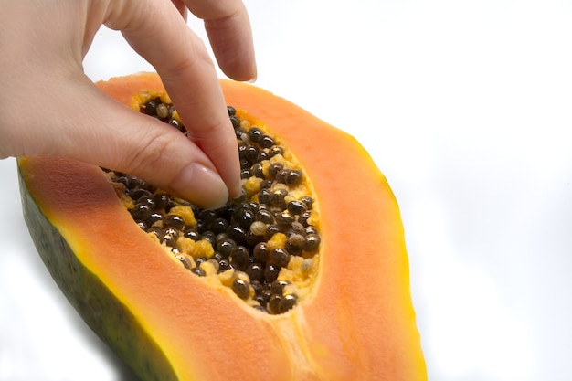 Frutta di papaia tagliata a metà con semi mano che tiene il seme isolato su sfondo bianco