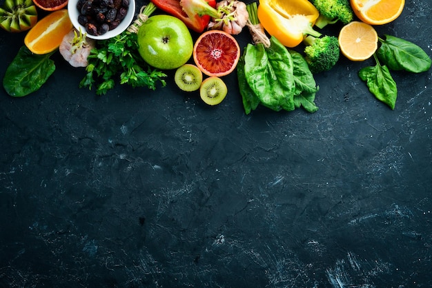 Frutta e verdura che contengono vitamina C Arancio limone mela rose aglio broccoli mela kiwi spinaci Vista dall'alto su sfondo di pietra nera