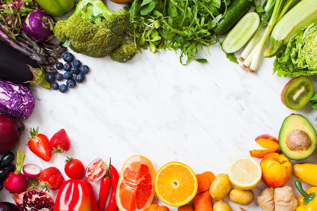 Frutta e verdura color arcobaleno come cornice su sfondo di marmo bianco. Posto per testo, concetto vegano e alimentazione sana