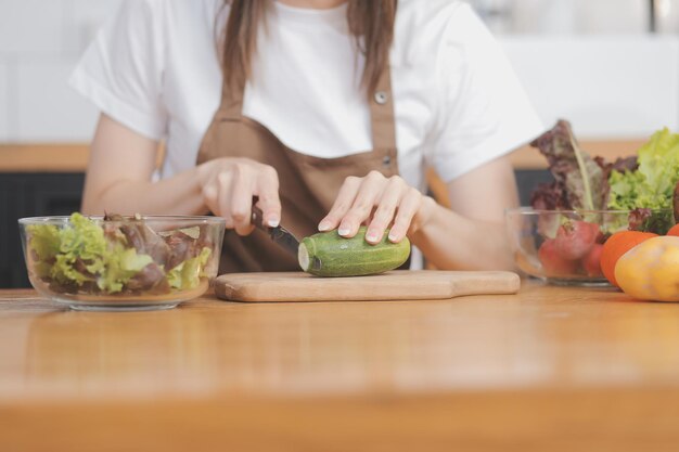 Frutta e verdura deliziose su un tavolo e donna che cucina la casalinga sta tagliando cetrioli verdi su una tavola di legno per fare insalata fresca in cucina