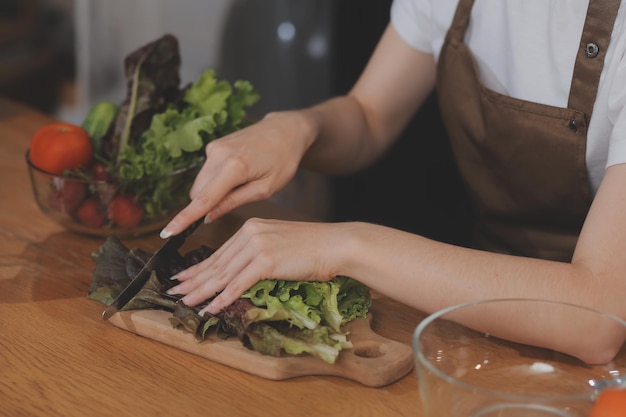 Frutta e verdura deliziose su un tavolo e donna che cucina la casalinga sta tagliando cetrioli verdi su una tavola di legno per fare insalata fresca in cucina