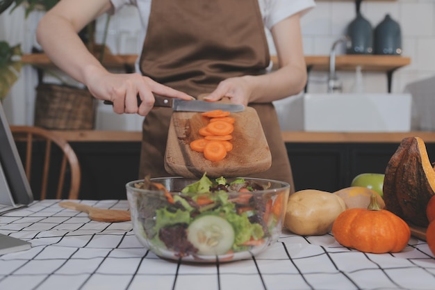 Frutta e verdura deliziose su un tavolo e donna che cucina la casalinga sta tagliando cetrioli verdi su una tavola di legno per fare insalata fresca in cucina