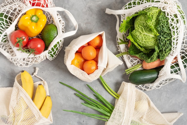 Frutta e verdura fresca in borse ecologiche tote su tavolo grigio vista dall'alto