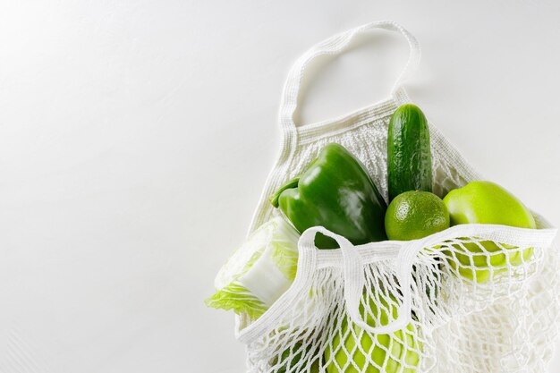 Frutta e verdura verdi in un sacchetto di corda bianco. Mele verdi, lime, cetrioli, peperoni e cavoli in un sacchetto di cotone riutilizzabile su uno sfondo bianco. Rifiuti zero concetto. Copia spazio