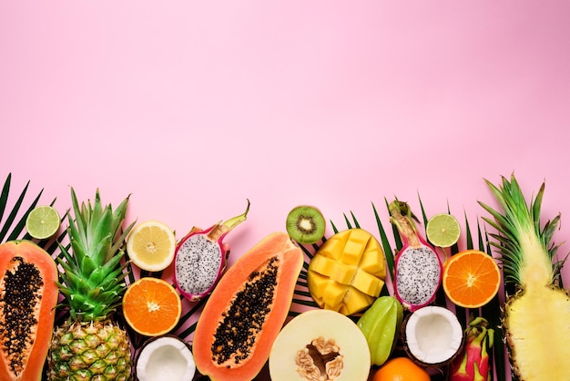 Frutta esotica e foglie di palma tropicali su sfondo rosa pastello papaia mango ananas banana carambola dragon fruit kiwi limone arancia melone cocco lime Vista dall'alto