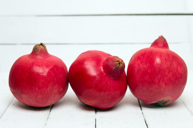 Frutta fresca del melograno isolata su un fondo di legno bianco.