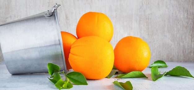 Frutta fresca di molte arance nel cestino dell'acciaio inossidabile e versare sullo sfondo di legno bianco