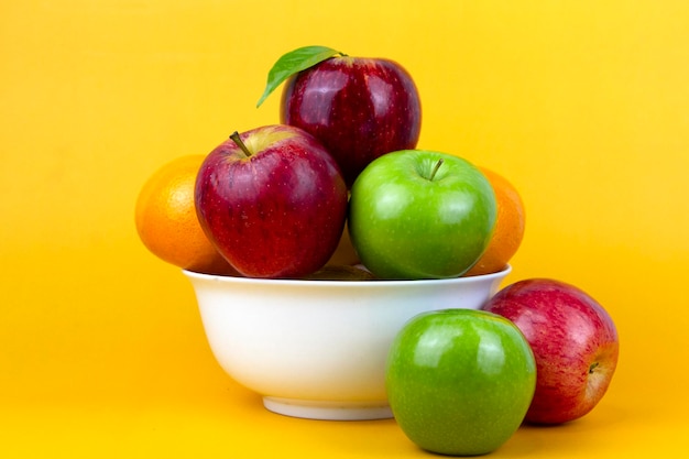 Frutta fresca e salutare mele verdi arance mela rossa isolate su sfondo giallo Frutti sani in una ciotola bianca su sfondo giallo utilizzata per cucinare annunci concettuali