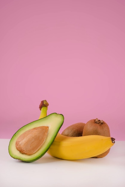 Frutta fresca su un tavolo - avocado a fette, banana, kiwi isolato su sfondo rosa