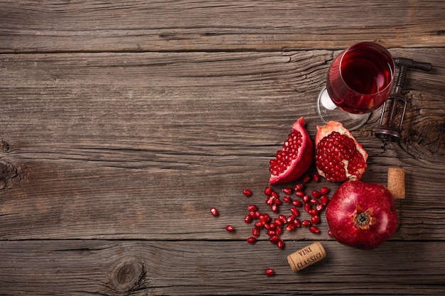 Frutta matura del melograno con un bicchiere di vino e una cavaturaccioli su un fondo di legno