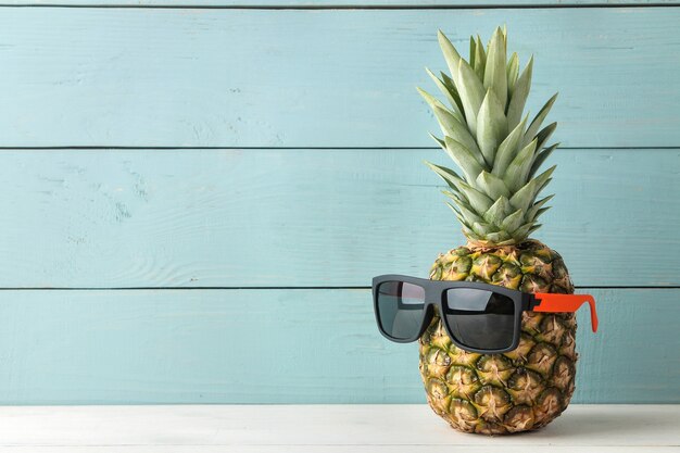 Frutta matura dell'ananas in occhiali da sole su una tavola di legno blu. posto per il testo.