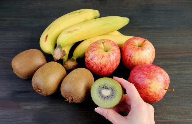 Frutta matura fresca assortita su fondo di legno nero con la mano che tiene un kiwi tagliato