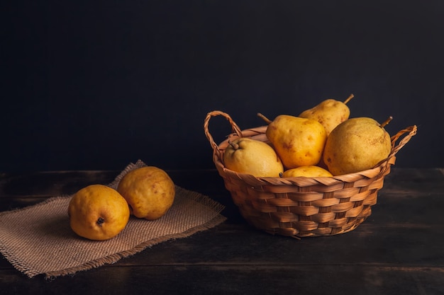 Frutta pera naturale con difetti in un cesto su un tovagliolo di iuta e uno sfondo di legno scuro.