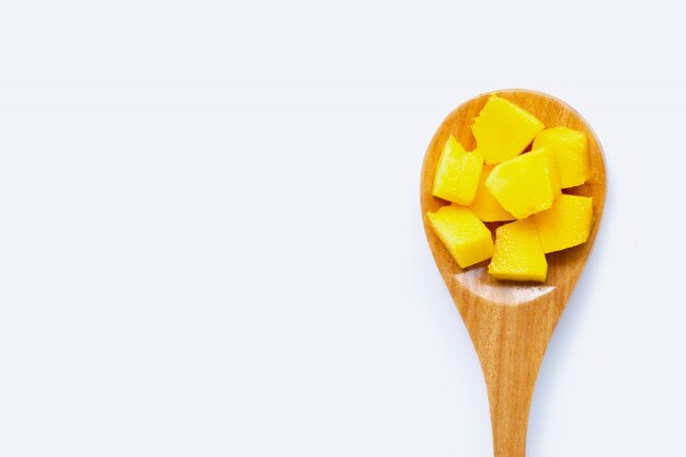 Frutta tropicale, fette del cubo del mango con il cucchiaio di legno su fondo bianco.