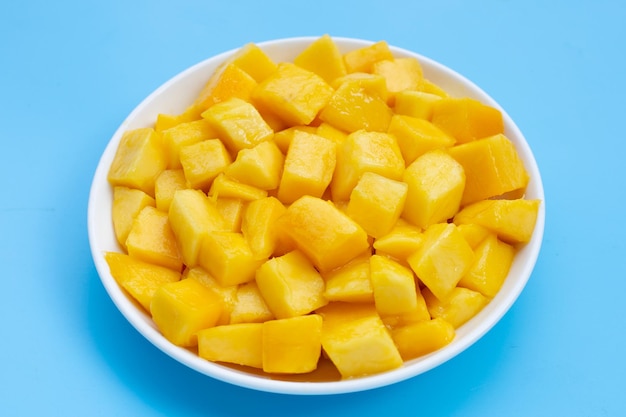 Frutta tropicale, fette di cubo di mango in ciotola bianca su sfondo blu.