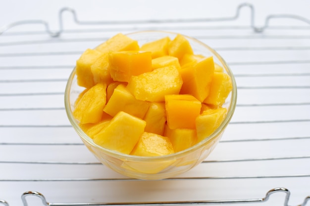 Frutta tropicale, fette di cubo di mango in ciotola di vetro su sfondo bianco.