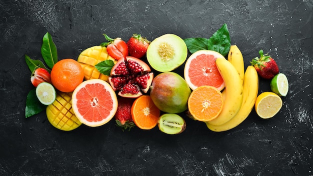 Frutta tropicale fresca su sfondo nero Agrumi melone melograno fragola banana Vista dall'alto Spazio libero per il testo