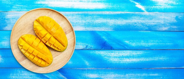 Frutta tropicale, mango in piatto di legno su fondo di legno blu.