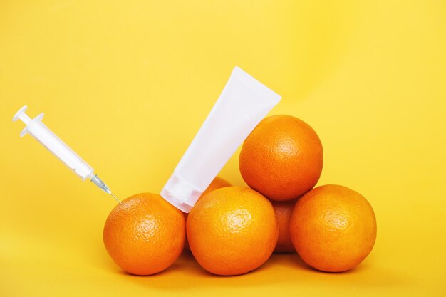 Frutti arancioni con siringa estraendo liquido con vitamina C e tubo crema vuoto