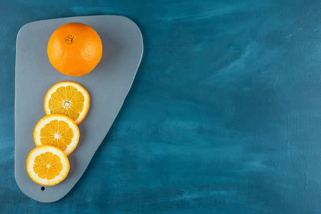 Frutti arancioni interi e affettati posti su un tavolo blu scuro.