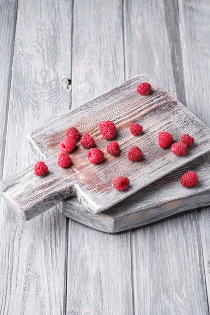 Frutti di lampone sul vecchio tagliere, mucchio sano di bacche estive sul tavolo di legno grigio, angolo di visione