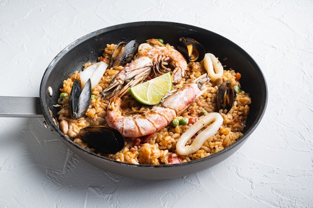 Frutti di mare e paella di pollo con riso, cozze, gamberetti, pollo, pomodori e vino in padella su sfondo bianco con texture