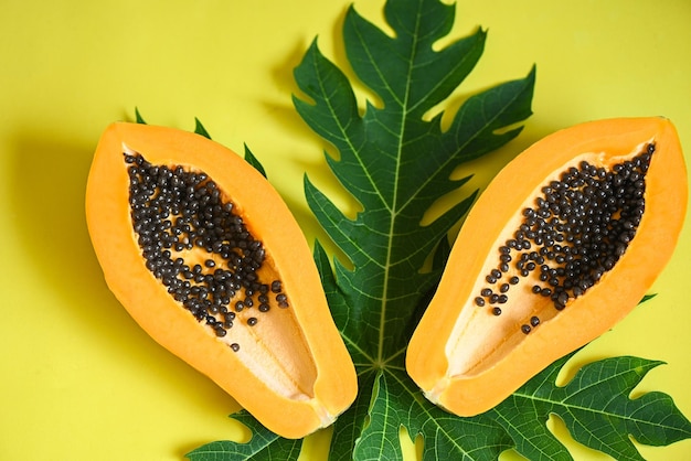 Frutti di papaia su sfondo giallo fetta di papaia matura fresca frutta tropicale con semi di papaia e foglie di foglie dell'albero di papaia