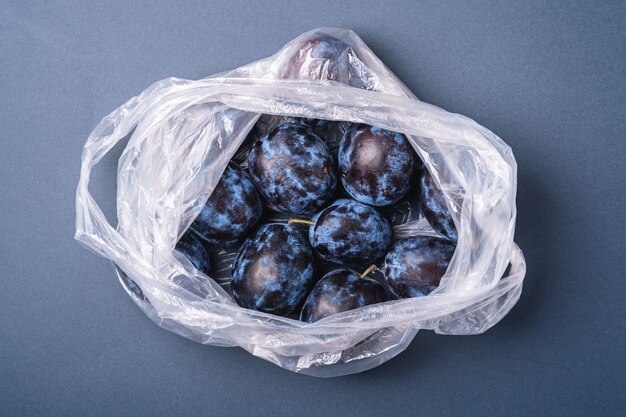 Frutti di prugna freschi maturi nel pacchetto del sacchetto di plastica su sfondo grigio blu minimo, vista dall'alto