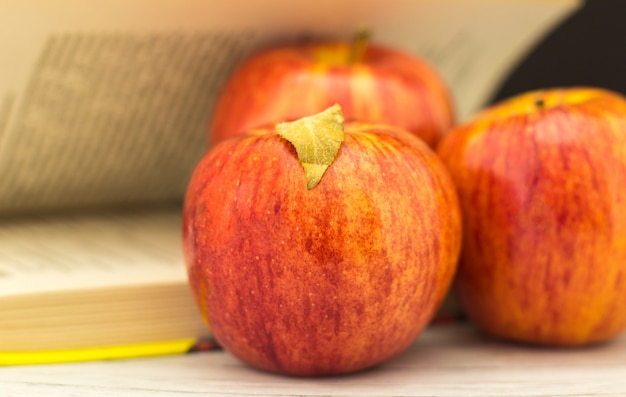 Frutti di una mela rossa con foglie vicino a un libro aperto