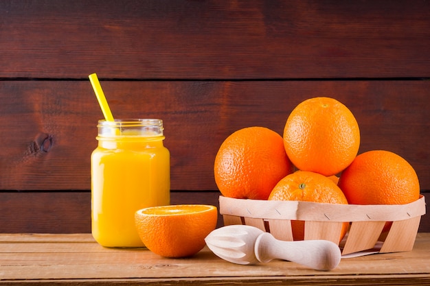 Frutti e succo d'arancia sui bordi di legno. Agrumi per fare il succo con spremiagrumi manuale. Arance in scatola di legno. Barattolo di vetro con succo d'arancia