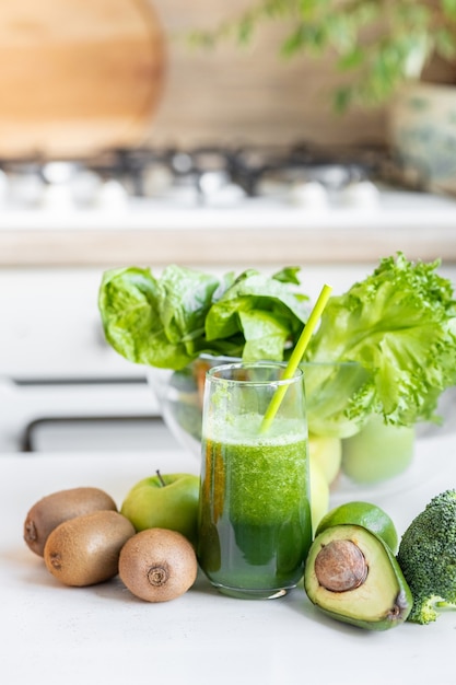 Frutti e verdure verdi maturi gustosi sul tavolo della cucina con un bicchiere e un frullatore
