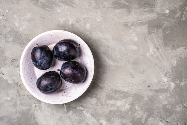 Frutti maturi freschi della prugna con gocce d'acqua nella ciotola di legno su priorità bassa del calcestruzzo di pietra, spazio della copia di vista superiore