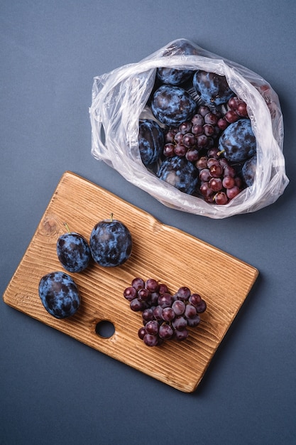 Frutti maturi freschi della prugna e bacche dell'uva nel pacchetto del sacchetto di plastica e sul tagliere di legno