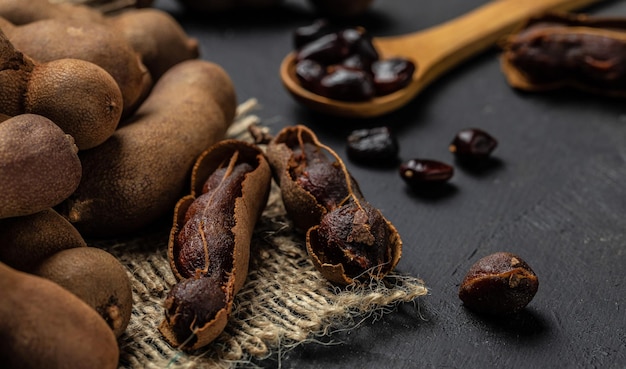 Frutti tropicali Fagioli di Tamarindo in guscio su un blocco di macellai marrone su uno sfondo scuro menu banner di frutta sana ricetta posto per testo vista dall'alto